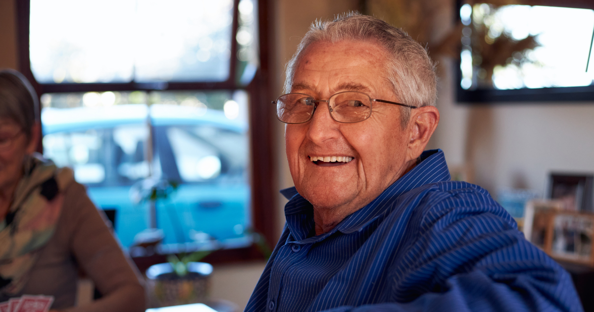 A smiling senior man sitting at a table, happy, as a result of successful long-distance caregiving.