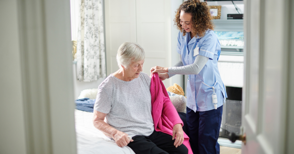 A professional caregiver helps a senior client get her coat on and get ready for the day.