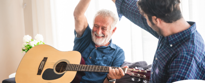 A smiling son high fives his happy elderly father as he plays the guitar, showing the positive effect music can have on people, including those with dementia.