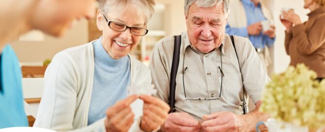 An older couple works on a puzzle with a caregiver, representing the kind of activity that helps those with dementia and also representing Alzheimer’s and Brain Awareness Month.