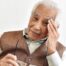 An older adult holds his head and his glasses representing vision problems like macular degeneration.