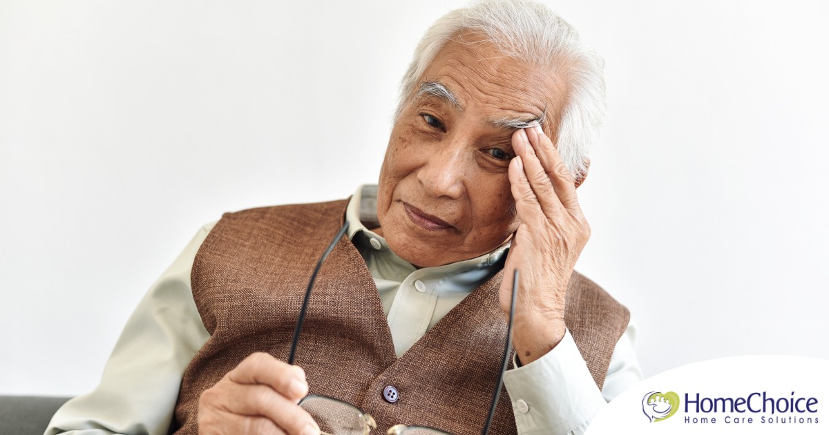 An older adult holds his head and his glasses representing vision problems like macular degeneration.