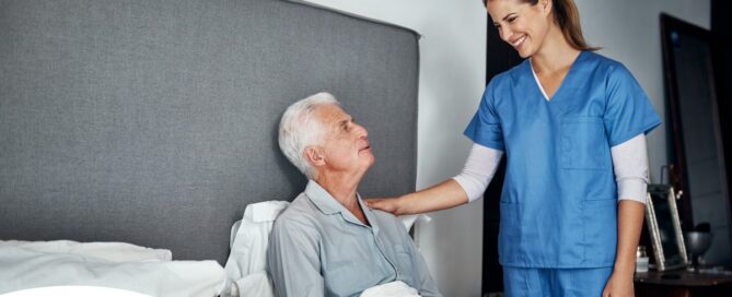 A caregiver smiles at an older client in bed, representing the compassion involved in being a live-in caregiver.