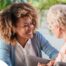A caregiver smiles at an older client in a chair, representing the joy that can come from a healthy work-life balance.