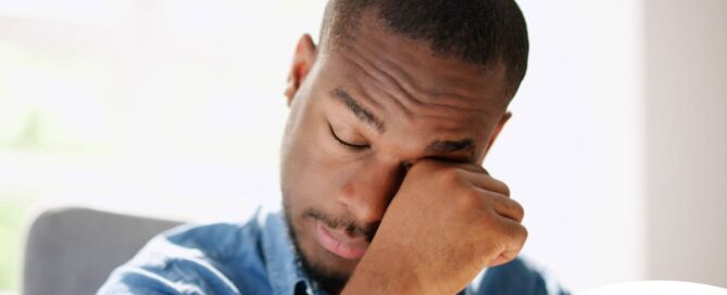 A man tiredly rubs his eyes, representing the exhaustion that can come with family caregiving.