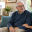 Home caregiver talking with an older man in a bright living room while providing supportive Parkinson’s home care.