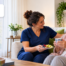 HomeChoice caregiver in navy scrubs sharing a healthy snack with a woman recovering from breast cancer at home with home care support.