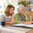 An older woman and her adult daughter review long term care insurance paperwork with a HomeChoice care professional at a table in their home.